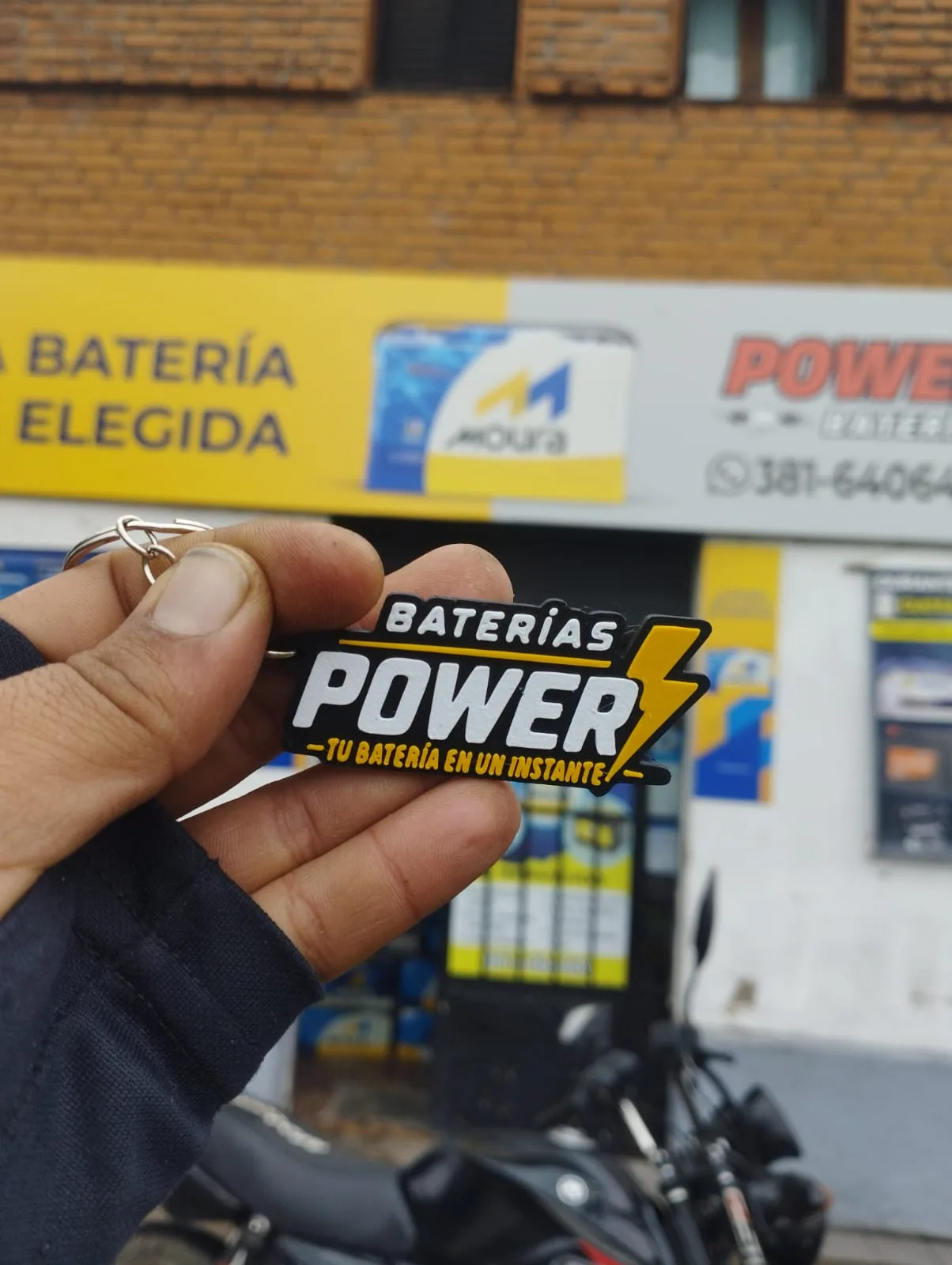 Llavero original con el logotipo de Baterías Power frente al local